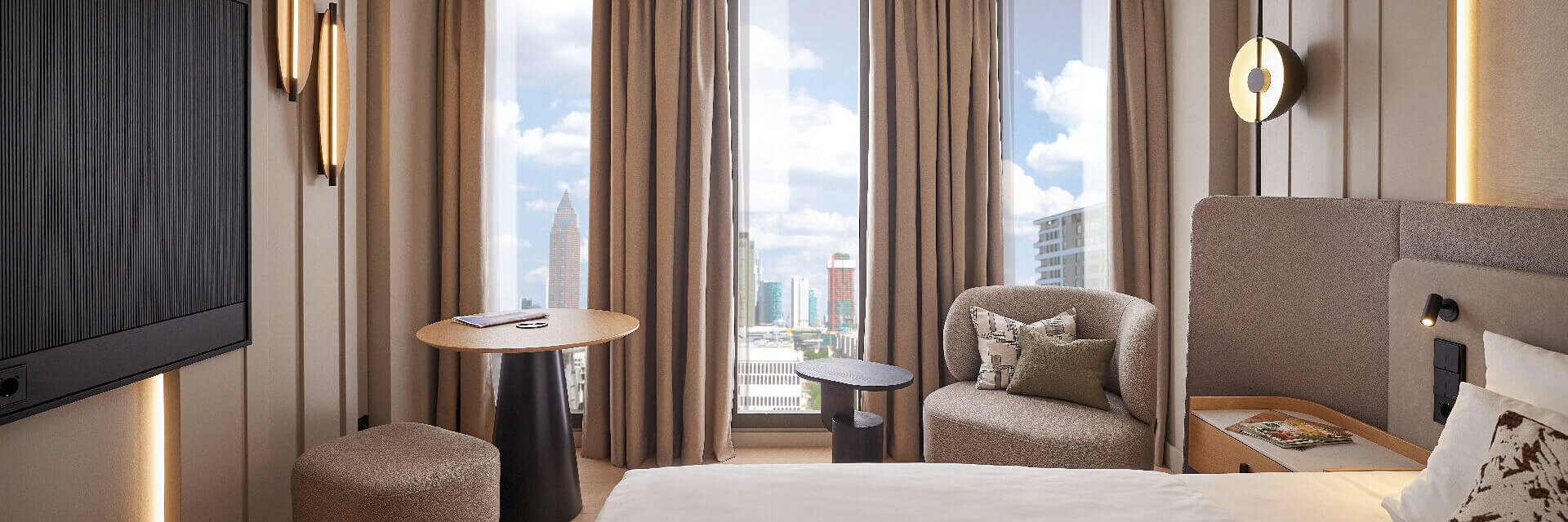Modern eingerichtetes Hotelzimmer im ATLANTIC Hotel Frankfurt mit großem Bett, Sitzbereich mit Sessel und kleinem Tisch sowie bodentiefen Fenstern, durch die eine Stadtansicht mit Hochhäusern zu sehen ist.