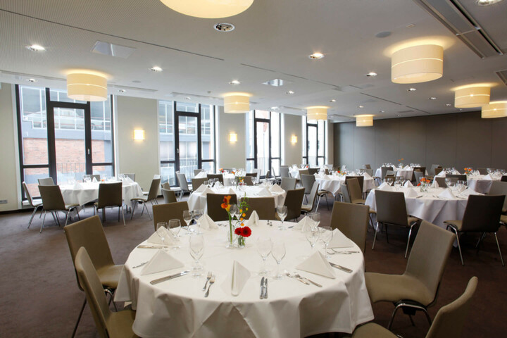 Eleganter Bankettsaal im ATLANTIC Hotel Lübeck mit runden, weiß gedeckten Tischen und modernen Stühlen.
