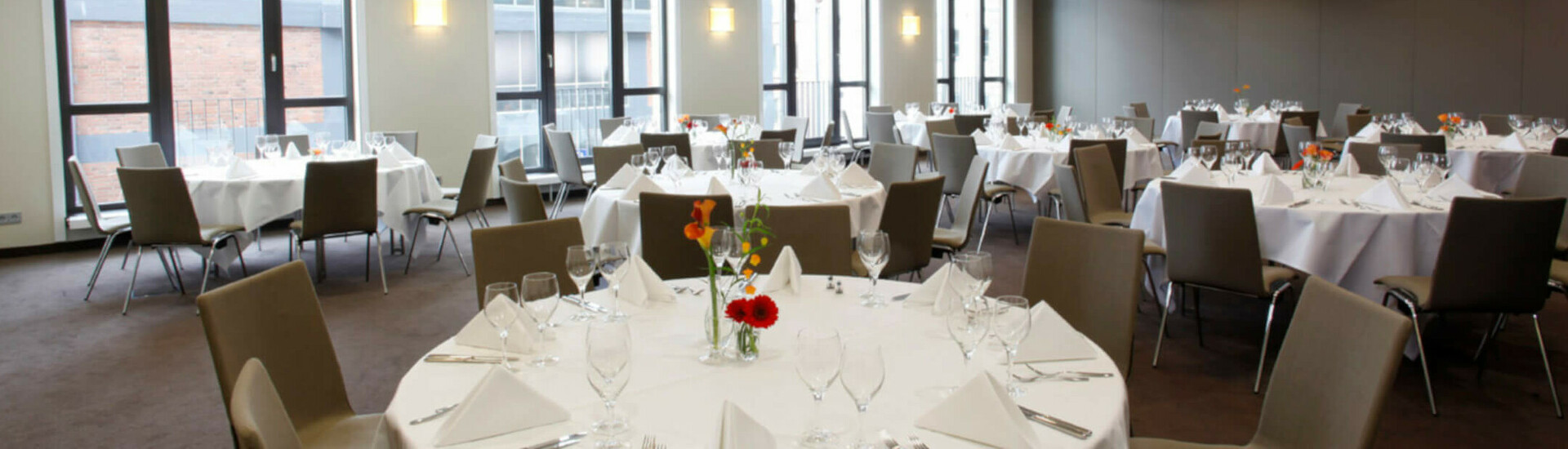 Eleganter Bankettsaal im ATLANTIC Hotel Lübeck mit runden, weiß gedeckten Tischen und modernen Stühlen.