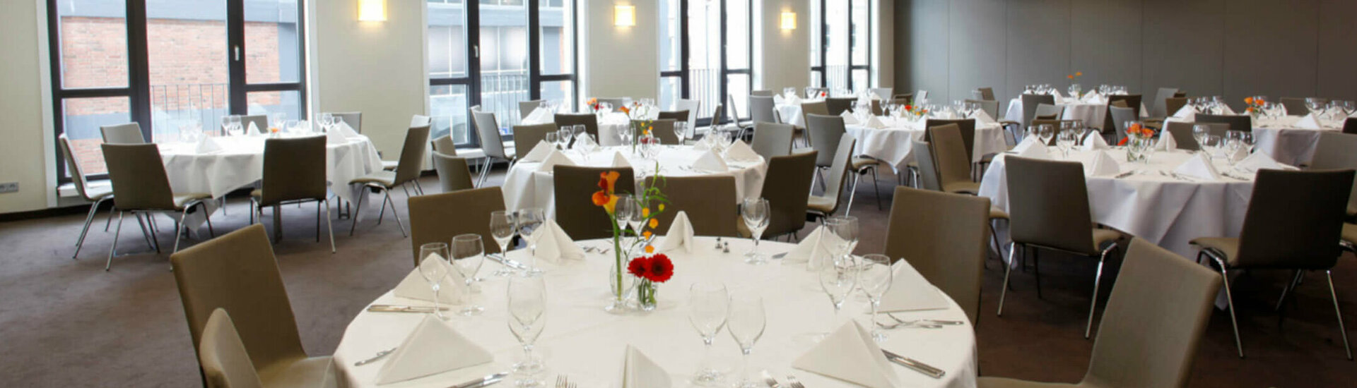 Function room at ATLANTIC Hotel Lübeck Elegant banquet hall in the ATLANTIC Hotel Lübeck with round tables set in white and modern chairs.