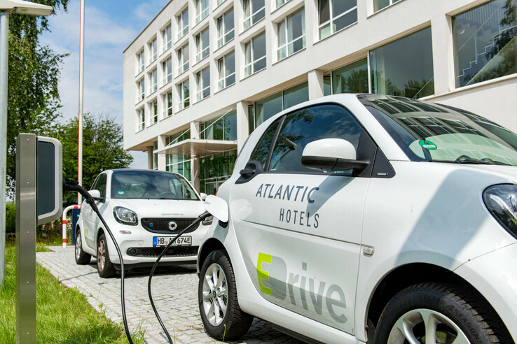 Two electric cars charging in front of a modern hotel building with large windows.