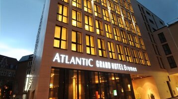Modernes Hotelgebäude bei Dämmerung, mit beleuchteten Fenstern und dem Schriftzug "ATLANTIC Grand Hotel Bremen".