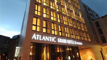 Exterior view of the ATLANTIC Grand Hotel in Bremen at twilight Modern hotel building at dusk, with illuminated windows and the lettering "ATLANTIC Grand Hotel Bremen".
