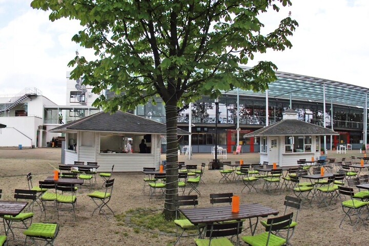 Our biergarten in the ATLANTIC Hotel Galopprennbahn Outdoor area of the ATLANTIC Hotel with tables, chairs and two pavilions, surrounded by trees.