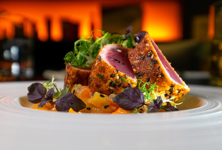 Gourmet dish with sesame tuna, fresh herbs and vegetables on a white plate, atmospheric lighting.