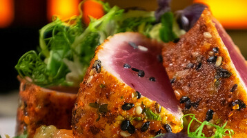 Gourmet dish with sesame tuna, fresh herbs and vegetables on a white plate, atmospheric lighting.