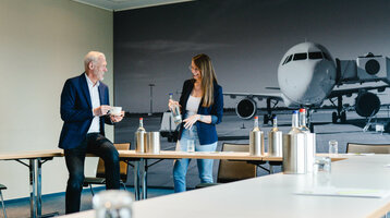 Two people in a conference room at the ATLANTIC Hotel Airport Bremen, with a picture of an airplane in the background.