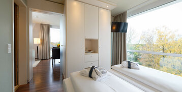 Bright hotel room with two single beds, large window and view of autumnal trees.