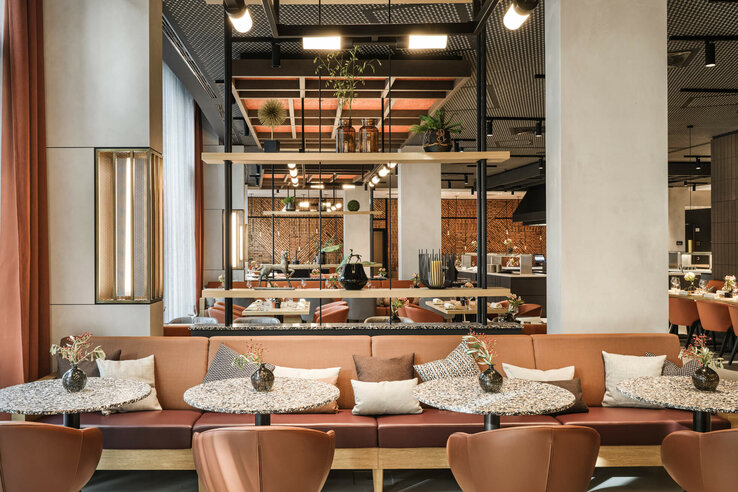 Modern hotel restaurant area with elegant tables, cozy benches, decorative plants and stylish lighting.