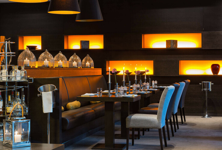 Elegantes Hotelrestaurant mit Kerzenlicht, modernen Möbeln und stilvoller Beleuchtung in warmen Orangetönen.