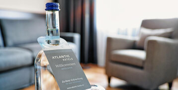 Flasche Wasser mit Willkommensschild im gemütlichen Hotelzimmer des ATLANTIC Hotel Landgut Horn Bremen.
