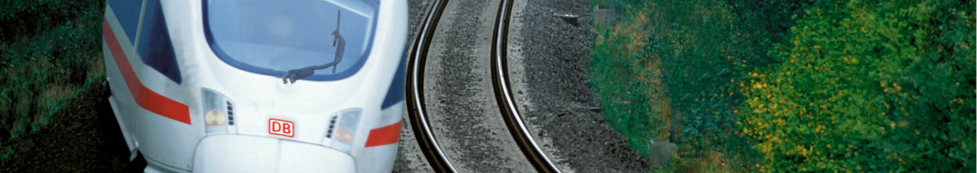 Ein ICE-Zug fährt auf einer kurvigen Schiene durch eine grüne, bewaldete Landschaft.