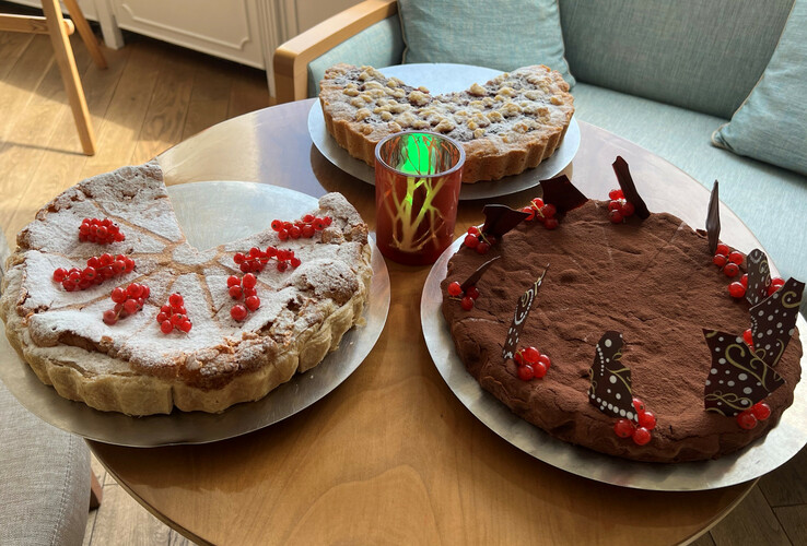 Three different cakes on a wooden table, decorated with red berries and pieces of chocolate.