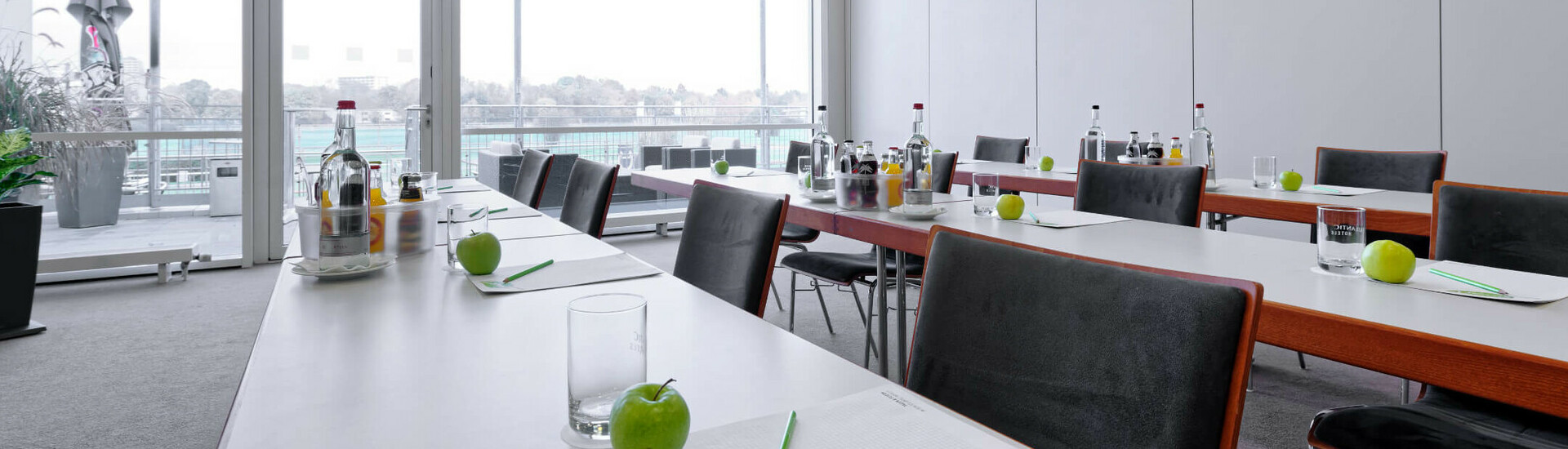 Meeting Raum mit parlamentarischer Bestuhlung Moderner Konferenzraum im ATLANTIC Hotel mit Tischen, Stühlen, Schreibutensilien und grünem Apfel, Blick auf Terrasse.