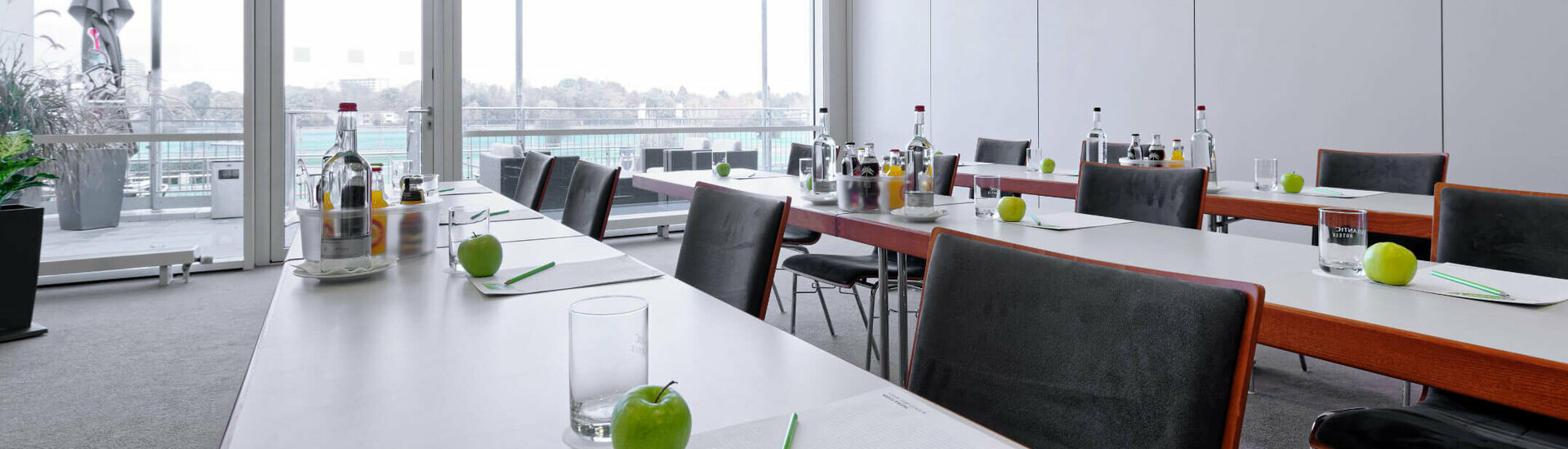Meeting room with parliamentary seating Modern conference room in the ATLANTIC Hotel with tables, chairs, writing utensils and green apple, view of the terrace.