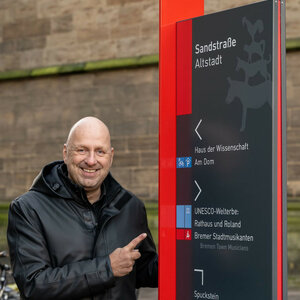 Leitsysteme in Bremen | ATLANTIC Hotel Bremen an der Galopprennbahn Ein Mann zeigt auf einen Wegweiser in der Altstadt mit den Bremer Stadtmusikanten als Symbol.