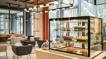 Deli Lounge in ATLANTIC Hotel Münster Cozy café in the ATLANTIC Hotel Münster with modern seating areas and a display case full of cakes and pastries.