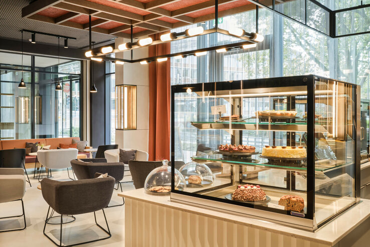 Cozy café in the ATLANTIC Hotel Münster with modern seating areas and a display case full of cakes and pastries.