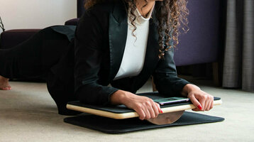 Frau in Businesskleidung macht Plank-Übung auf Balance-Board im modernen Hotelzimmer.