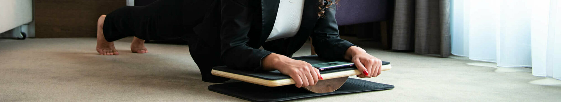 Plankpads in ausgewählten ATLANTIC Hotels verfügbar  Frau in Businesskleidung macht Plank-Übung auf Balance-Board im modernen Hotelzimmer.
