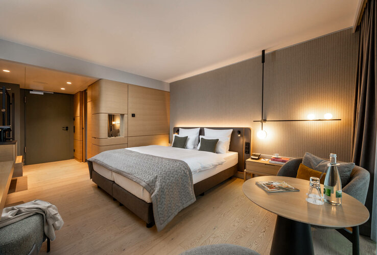 Modern hotel room with double bed, elegant lighting, seating area and wooden accents at the ATLANTIC Hotel Heidelberg.