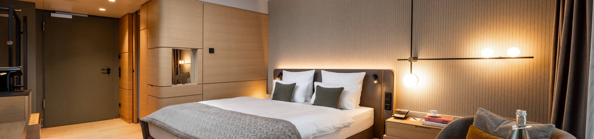 Modern hotel room with double bed, elegant lighting, seating area and wooden accents at the ATLANTIC Hotel Heidelberg.