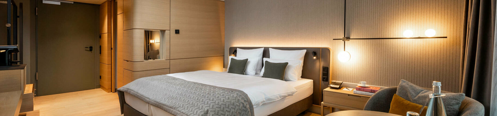 ATLANTIC Hotel Heidelberg Comfort Room Modern hotel room with double bed, elegant lighting, seating area and wooden accents at the ATLANTIC Hotel Heidelberg.