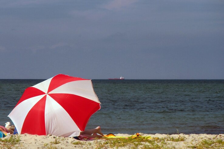 Beach with red parasol, sea and blue sky behind it, relaxed atmosphere.