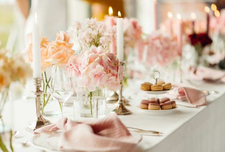 Eleganter Tisch mit rosa Blumen, brennenden Kerzen und Macarons im ATLANTIC Hotel Münster, festlich gedeckt.