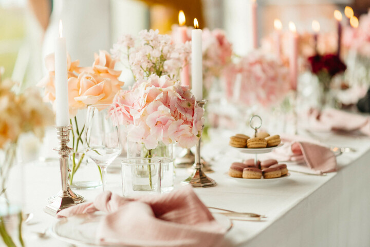 Weddingtable von "True Love Hochzeiten" im ATLANTIC Hotel Münster Eleganter Tisch mit rosa Blumen, brennenden Kerzen und Macarons im ATLANTIC Hotel Münster, festlich gedeckt.