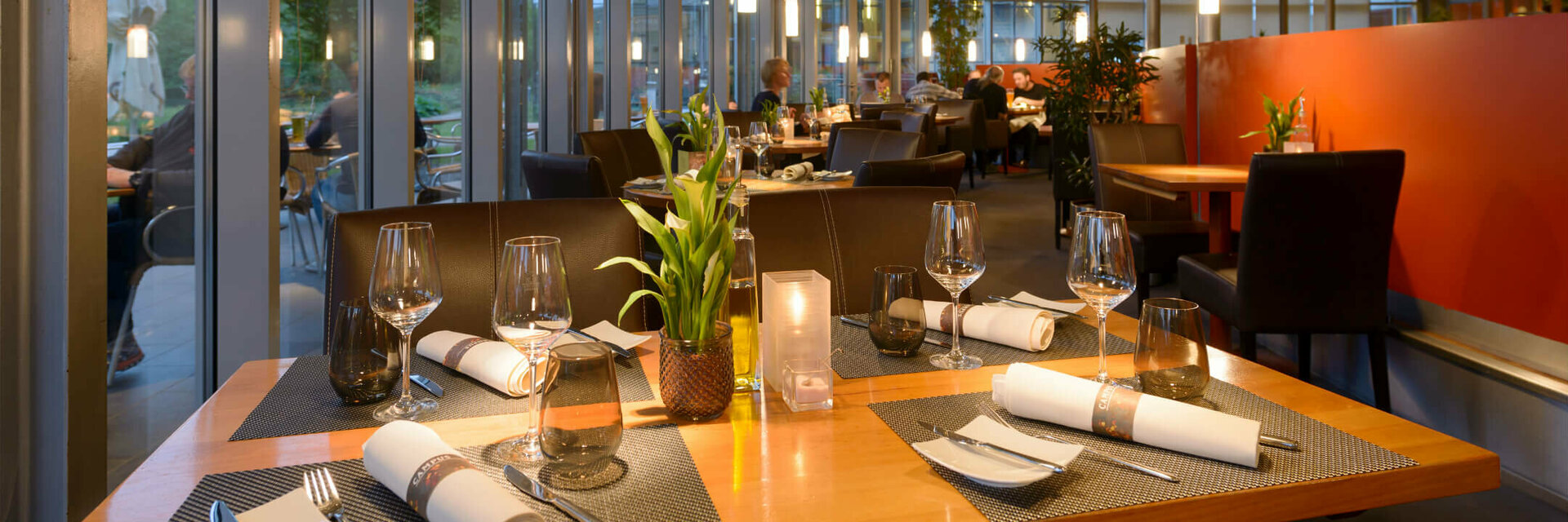 Modernes Hotelrestaurant mit gedeckten Tischen, großen Fenstern und stimmungsvoller Beleuchtung im ATLANTIC Hotel Universum.