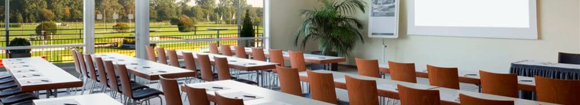 Heller Konferenzraum im ATLANTIC Hotel mit Reihen von Tischen, Stühlen und Blick auf grüne Wiesen.