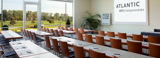 Heller Konferenzraum im ATLANTIC Hotel mit Reihen von Tischen, Stühlen und Blick auf grüne Wiesen.
