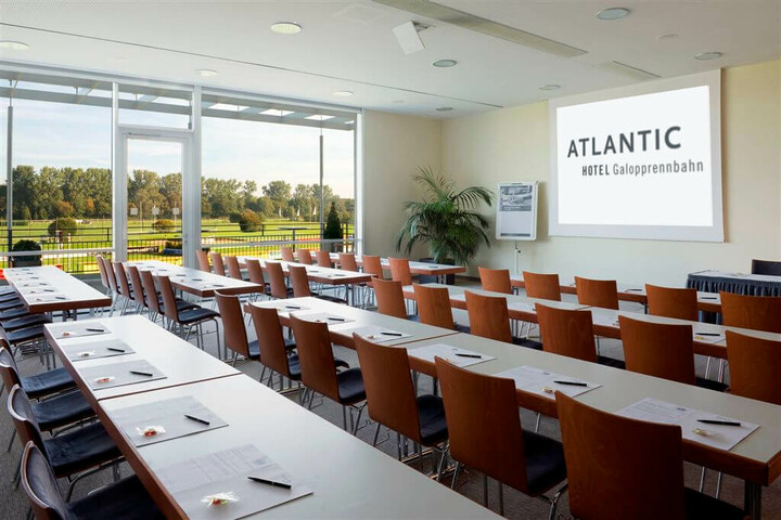 Heller Konferenzraum im ATLANTIC Hotel mit Reihen von Tischen, Stühlen und Blick auf grüne Wiesen.