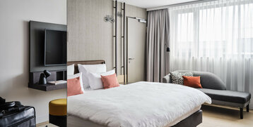 Modern hotel room at the ATLANTIC Hotel Münster with double bed, sofa, TV and large windows.
