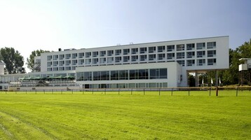 ATLANTIC Hotel Galopprennbahn in Bremen Modernes Hotelgebäude mit großen Fenstern, umgeben von grünem Rasen und Bäumen.