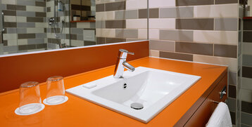 Modern bathroom in the ATLANTIC Hotel with orange vanity top, white washbasin and stylish tiles.