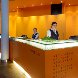 Rezeption des ATLANTIC Hotel Universum mit freundlichem Personal und modernem, orangefarbenem Design.