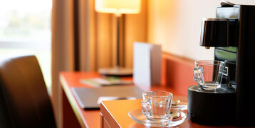Coffee machine with glasses on a desk in the ATLANTIC Hotel Galopprennbahn, warm lighting in the background.