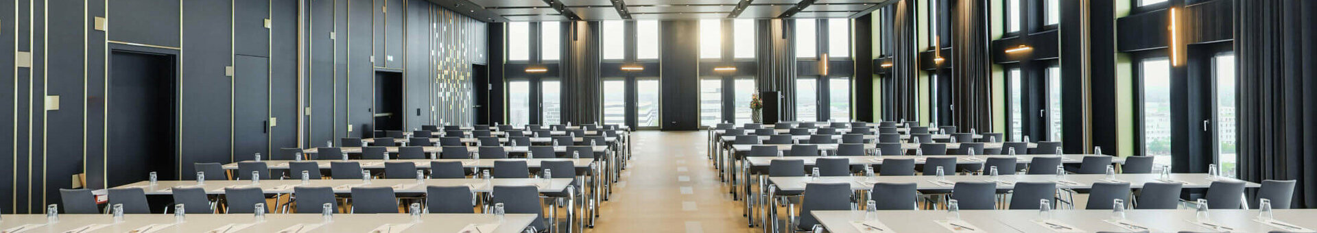 Moderner Konferenzraum im ATLANTIC Hotel Heidelberg mit Reihen von Tischen und Stühlen, großen Fenstern und eleganter Beleuchtung.