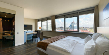 Modern hotel room with large window, double bed, desk and view of the Bremerhaven skyline.