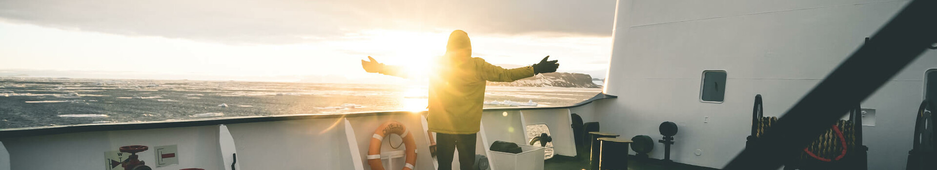 Film-Projekt Antarktis | Sponsoring durch ATLANTIC Hotel Sail City Bremerhaven Person auf Schiffdeck genießt Sonnenuntergang, mit ausgestreckten Armen, Meer im Hintergrund.