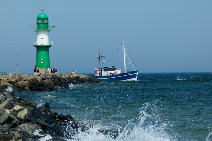 Grüner Leuchtturm auf Wellenbrecher, Fischerboot im Meer, blauer Himmel, ATLANTIC Grand Hotel Travemünde nahe Umgebung.