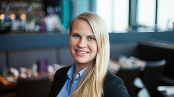 Ansprechpartner Leisure Sales Maike Seedorff | ATLANTIC Hotels Eine lächelnde Frau in Business-Kleidung steht in einem stilvollen Restaurant.