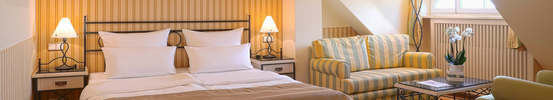 Cozy hotel room with double bed, sitting area, chandelier and skylight in the ATLANTIC Grand Hotel Travemünde.