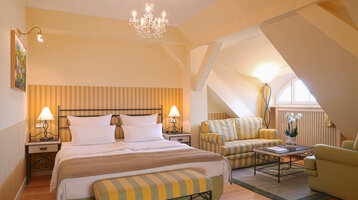 Cozy hotel room with double bed, sitting area, chandelier and skylight in the ATLANTIC Grand Hotel Travemünde.