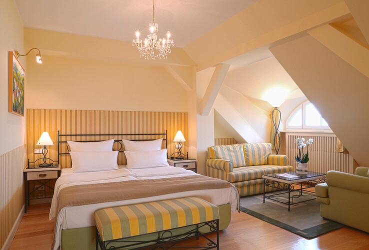 Cozy hotel room with double bed, sitting area, chandelier and skylight in the ATLANTIC Grand Hotel Travemünde.