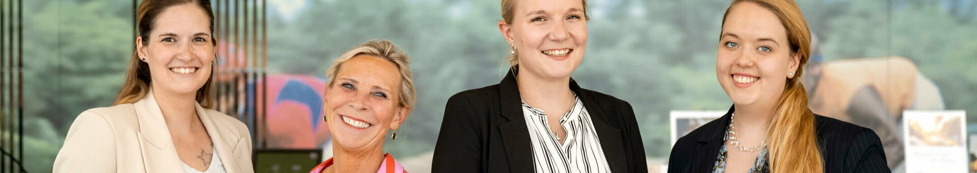 Four smiling women in business attire in front of a background with a nature motif at the ATLANTIC Hotel Galopprennbahn.