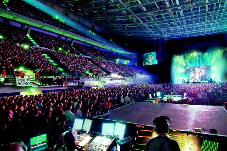 Large, well-attended concert arena with stage, colorful lights and sound mixer in the foreground.