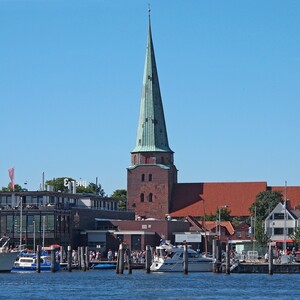 Hafenansicht mit Segelbooten, historischer Kirche und modernen Gebäuden bei klarem Himmel in Travemünde.
